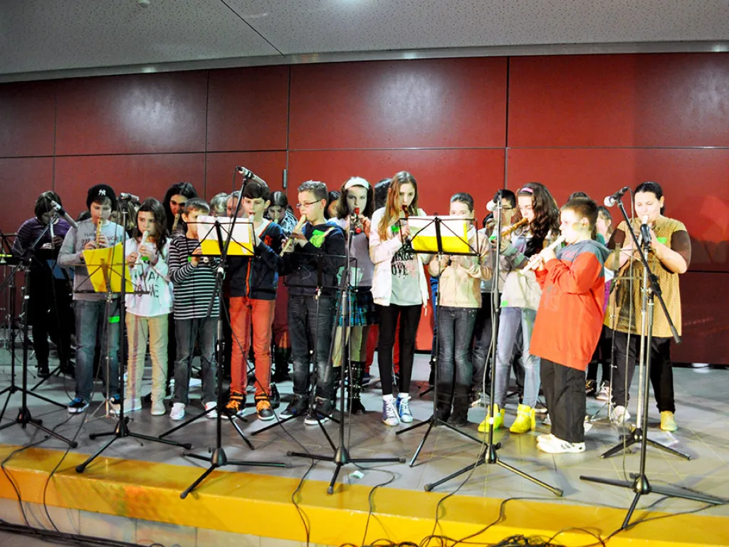 Chorgruppe singt an Mikrofonen vor der roten Wand.